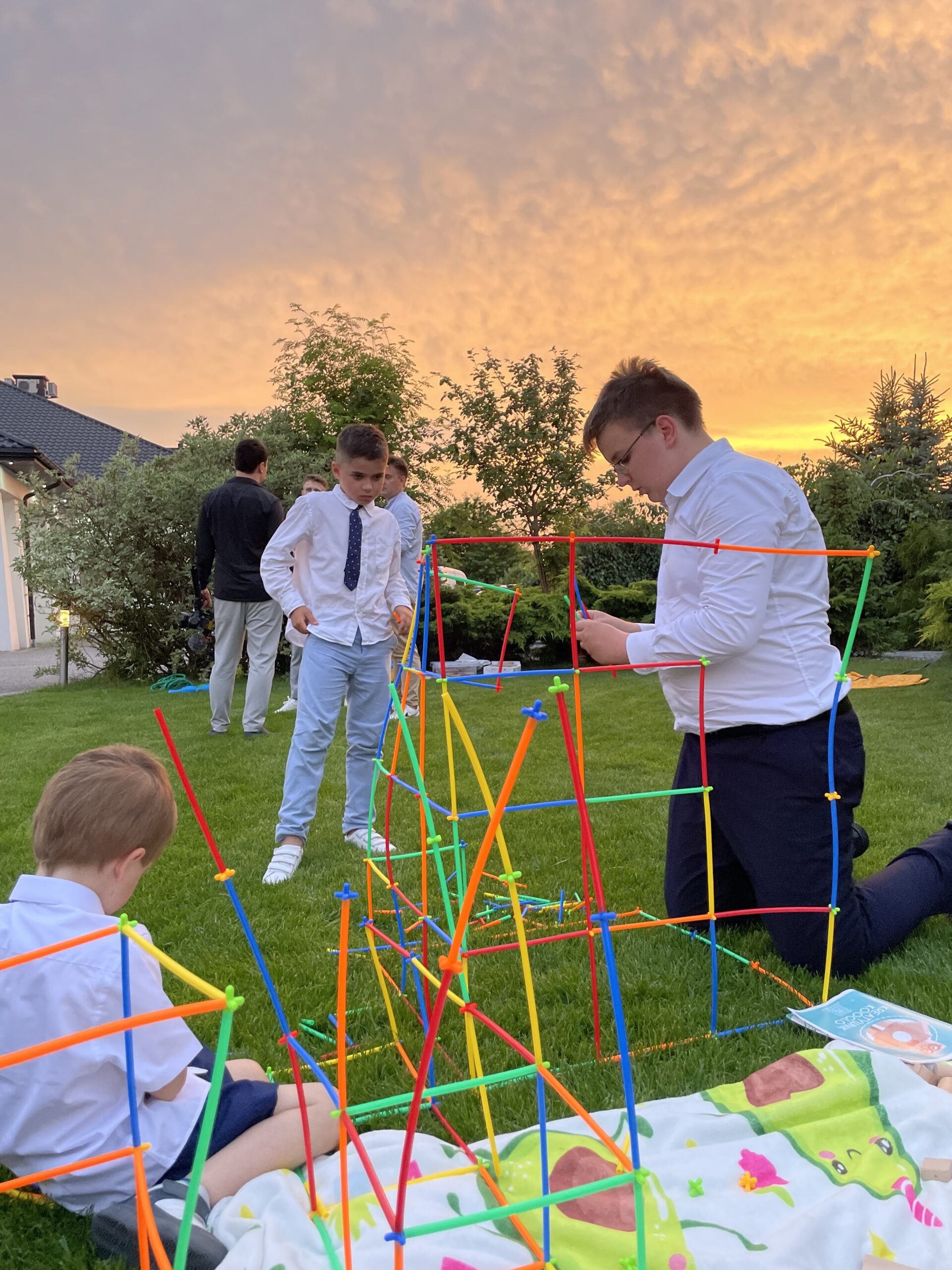 Dzieci budujące konstrukcję z klocków i rurek podczas animacji na weselu, w tle zachód słońca