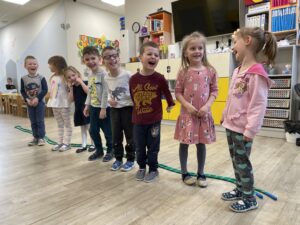 Uśmiechnięte dzieci biorące udział w zajęciach ruchowych z liną w przedszkolu.