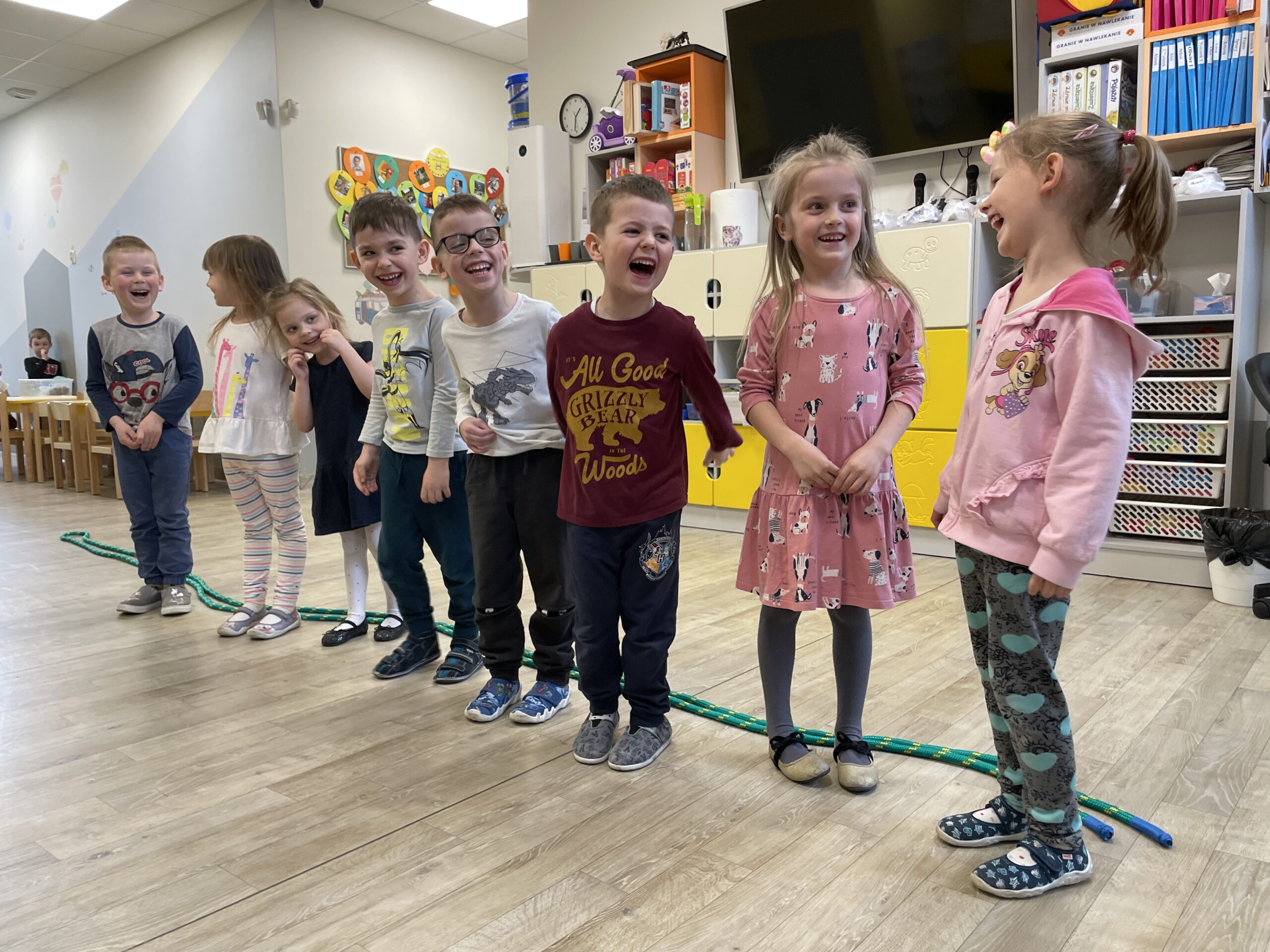 Uśmiechnięte dzieci biorące udział w zajęciach ruchowych z liną w przedszkolu.